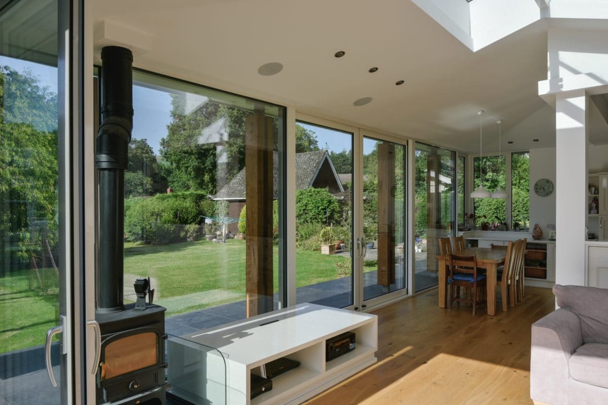 Interior of home extension. Interior shows three walls of glazing with a roof opening to create a light-filled living area. Inside is a fire place and coffee table, from this table will rise a tv. Communion architects, Herefordshire.