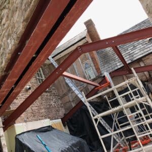 Angled photo of stone walls and supporting steel beams on a construction site for a new extension to a listed building in Herefordshire. Communion Architects.
