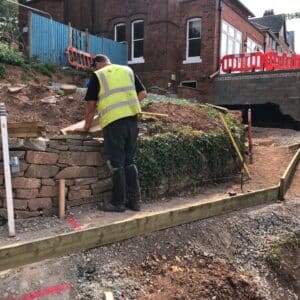 Construction worker in a hi-vis jacket measuring the level of a stone wall as part of some landscaping works in a garden in Hereford, Communion Architects
