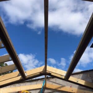 Looking towards a blue sky through a timber frame for an extension to a listed building. The gap in the roof will become a sky light. Communion Architects, Hereford