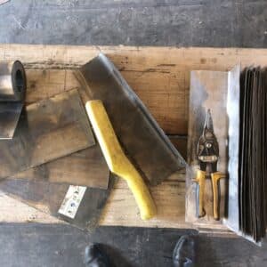A wooden bench with lead rolls and cutting tools - part of a roofer's kit - image from a construction site in Herefordshire, communion architects