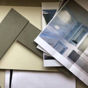 Two slender, angled tiles next to rendered bathroom plans on a workbench, planning out bathroom and tile design on site, communion architects Hereford