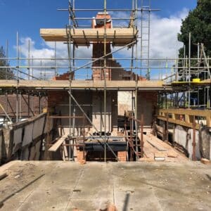 Standing on some access scaffolding looking across at a chimney being constructed at the far end of a cottage, it's covered in scaffolding and the thatch which should cover the roof has not yet been relaid since the fire. Re-building a fire damaged cottage in Worcestershire. communion architects Hereford.