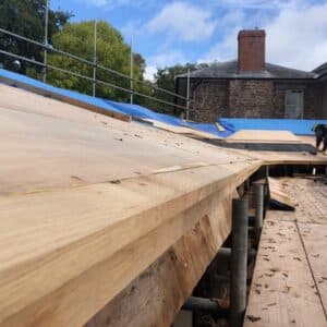 Perspective image on a long wooden roof truss taking up most of the image, it leads the viewer to a stone build house in the background, the new roof truss is part of extension works on the site. Communion Architects, Hereford
