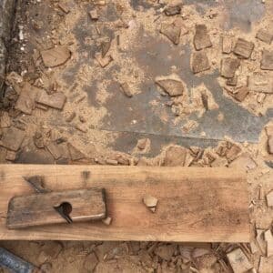 a short plank on wood laying on a grey concrete floor across the lower third of the image, the short plank is surrounded by wood chips, off cuts and saw dust. Communion Architects, Herefordshire.
