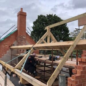 New oak roof truss partway completed on a red brick cottage, image taken from the scaffolding level with the roof trusses. Communion Architects, Hereford.