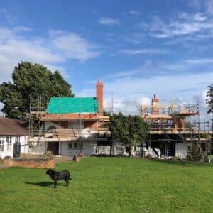 a old white washed cottage covered in scaffolding with a new roof in the process of being installed. Blue sky above and green grass below. Communion Architects, Hereford.