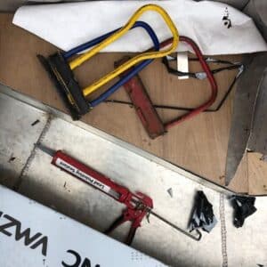 Zinc folding equipment and a sealant in a red sealant gun laying on a wooden planks and zinc sheets. Communion Design, Hereford.