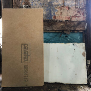 A board of insulation stands upright against a white plaster board behind it, with a fire damaged timber frame behind them both. Part of repairs to a fire damaged cottage, creating breathable construction to protect the historic fabric. Communion Architects, Hereford, Herefordshire.