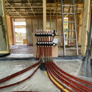 A timber framed structure under construction. at the centre of the image is a ground source heat pump with several red wires spreading out from it across the floor. Communion Architects Hereford, Herefordshire.