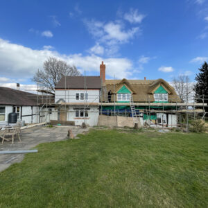 A L shaped black and white cottage with scaffolding, with a new thatched roof, complete with a decorative ridge.