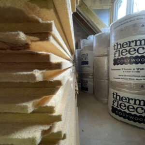 The left hand side shows a pile of flat layers of insulation. To the right hand side, the insulation is wrapped in round plastic bundles labelled 'thermal fleece'. Communion Architects, Hereford, Herefordshire.