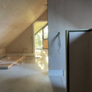 inside an attic room with sloping roof and freshly plaster walls. The end wall is glazed with golden autumnal sun shine through. New House designed by communion architects Hereford