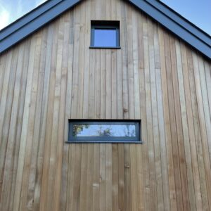 End wall of a new house, a pet slate roof, facade is boarded with fresh cedar. Communion Architects Hereford