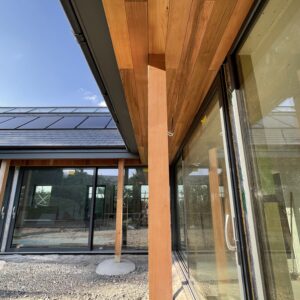 L-shaped house - close up of timber columns and timber eaves supporting an overhanging roof, protecting a wall of glass, communion architects Hereford.