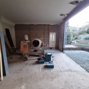 A concrete mixer and building tools sitting in the centre of large room which is open to the garden. Its the creation of a new family space awaiting the installation of glazed doors. Communion Architects Hereford