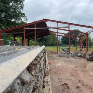 A red steel framed structure in the middle of a field. Communion Architects Hereford