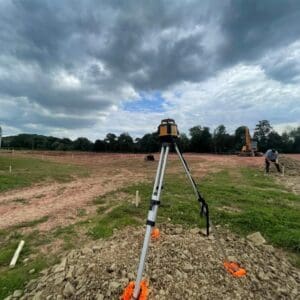 An open field in the countryside with a camera set up on a tripod for site survey. Communion Architects Hereford