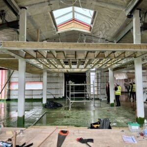 The interior of a steel framed construction showing steel timbers, a raised mezzanine platform and large glazed skylight. Communion Architects Hereford