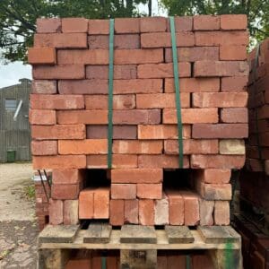 A large pile of red bricks stacked on a wooden palett. Communion Architects Hereford